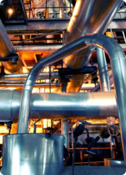 Industrial piping and process equipment used in manufacturing, utilities, and plant operations. Metal pipes and ducts in an industrial setting with people in the background