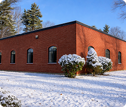 Load Controls company facility and headquarters building during winter snowfall. Red brick building with snow on the ground and trees in the background