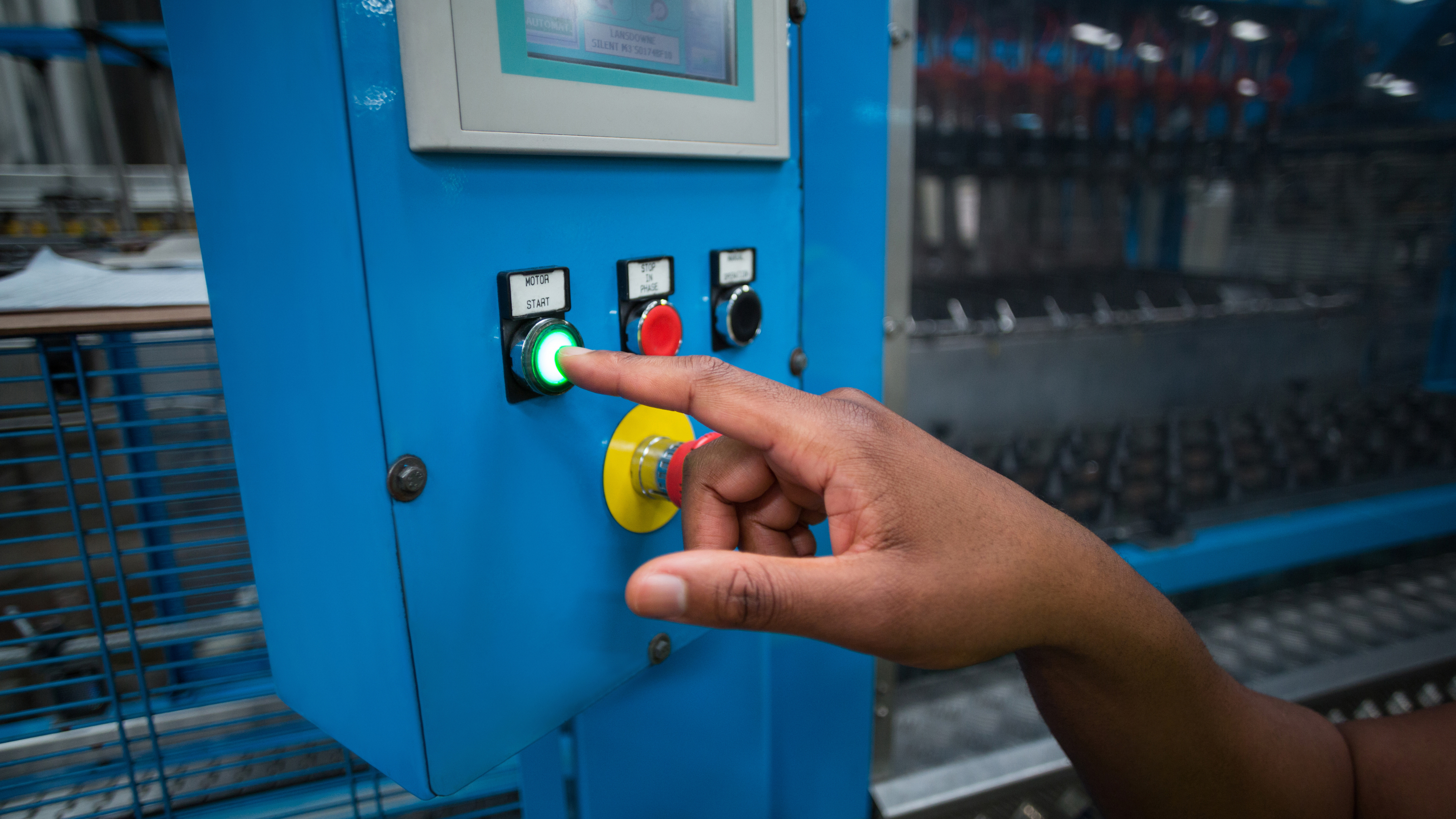 Hand pressing a button on a blue control panel with various buttons.